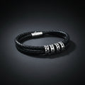 A black braided leather bracelet with silver-toned cylindrical beads featuring white lettering, displayed on a clean white background.