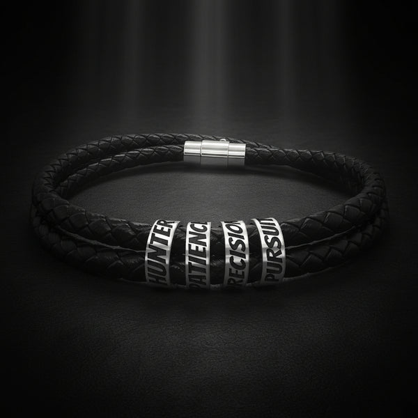 A black braided leather bracelet with silver-toned metal spacers engraved with words including HUNTER, MATHEMATICS, PRECISION, and PURSUIT.